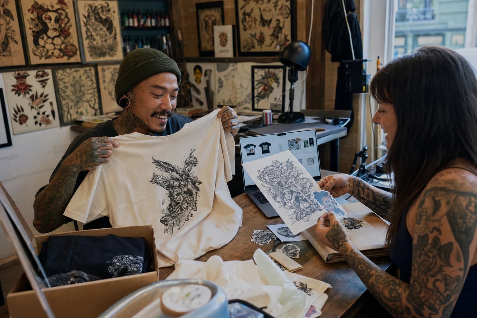 Tattoo artists reviewing print-on-demand shirts, art prints, and storefront proofs